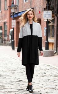 Woman wearing a long black and gray cardigan on a cobblestone street.