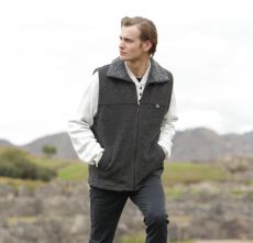 Man in a black vest and white shirt standing outdoors in a natural setting.