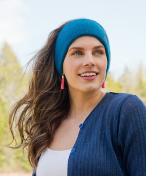 A young woman with long hair wearing a blue headband and sweater outdoors.