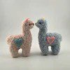 Two small crocheted alpacas facing each other, one beige and one blue with a heart.