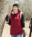 Person wearing a red vest and black gloves in a wooded area.