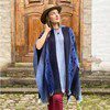 Woman in a blue shawl and hat standing by a wooden door.