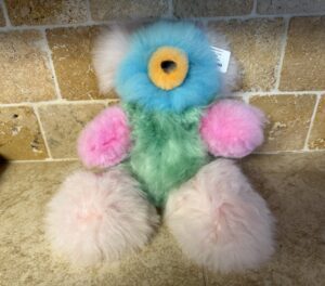 A colorful plush toy with fluffy limbs and a single large eye.