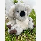 A fluffy stuffed koala toy sitting on green grass.