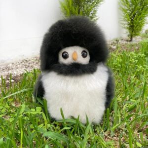 A cute penguin plush toy with a fluffy black head and white belly sits on grass.