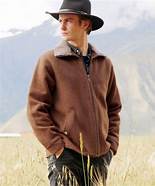 Man wearing a brown jacket and black hat standing in a grassy field.