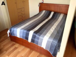 A neatly made bed with a striped blue and gray blanket in a wooden bedroom.